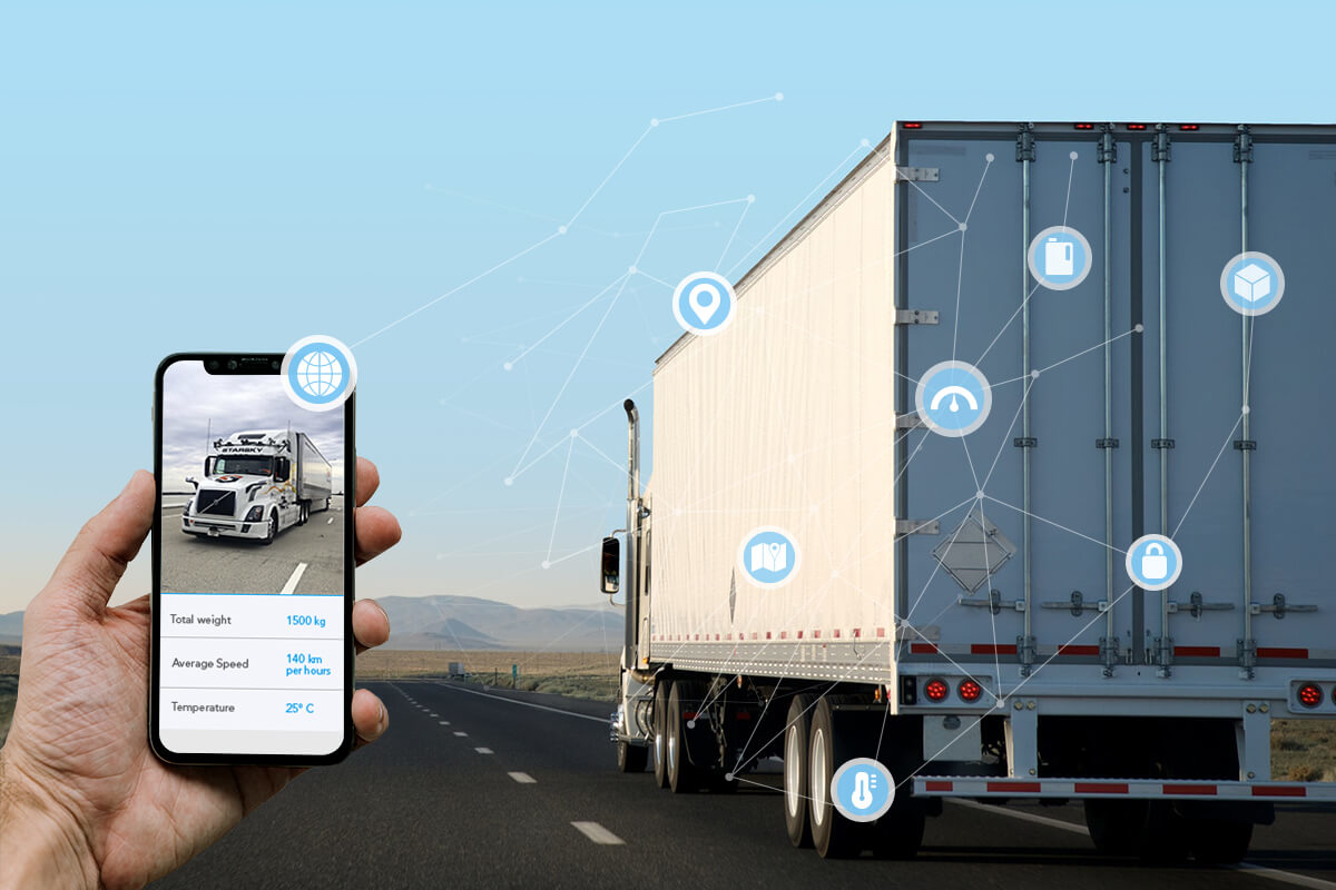 Hand holding smartphone showing truck tracking app beside semi-trailer truck on highway.