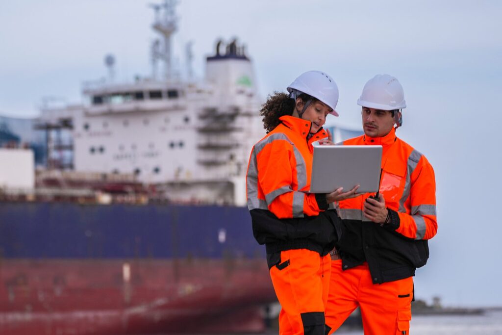 Port logistics workers in hi-vis gear reviewing cargo on a laptop